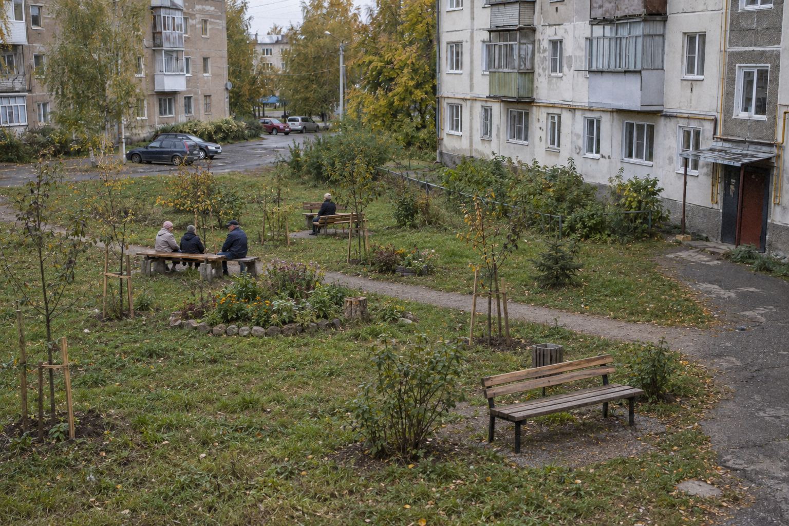 На месте пустыря — зелёный уголок с саженцами, клумбой и лавочками, на скамейке сидят соседи